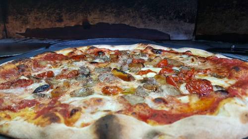 A freshly baked pizza with melted cheese, sausage, and roasted tomatoes, resting on a stone surface.