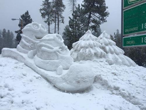 A large snow sculpture of a frog on a sled, surrounded by snow-covered trees.