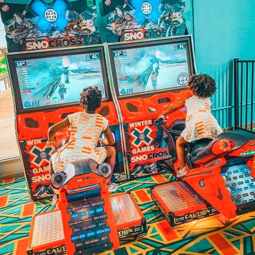 Two children playing snowmobile racing arcade games, focused on the screens in a colorful gaming area.