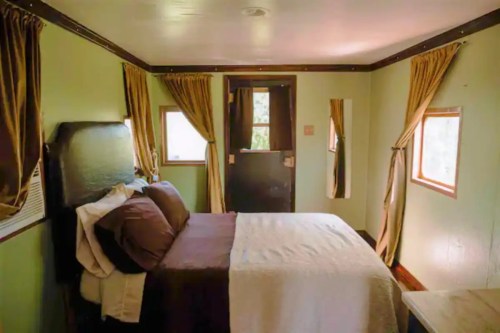 Cozy bedroom with a bed, brown and white bedding, green walls, and curtains, featuring two windows and a door.