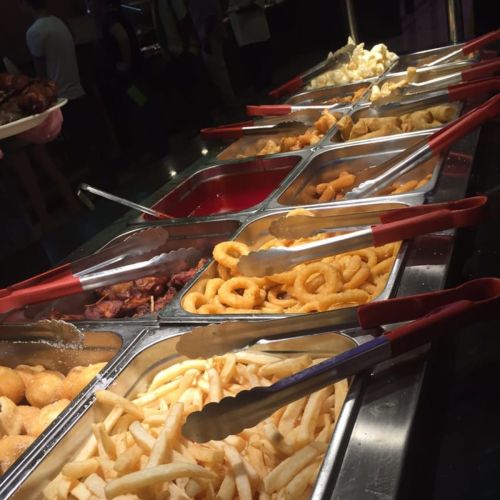 A buffet display featuring various fried foods, including fries, onion rings, and other snacks in metal trays.