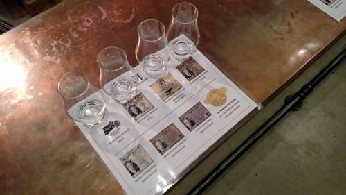 A table with four glasses and a tasting menu featuring various whiskey labels and descriptions.
