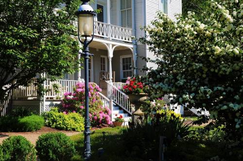 A charming house with a porch, surrounded by colorful flowers and greenery, with a vintage lamp post in the foreground.