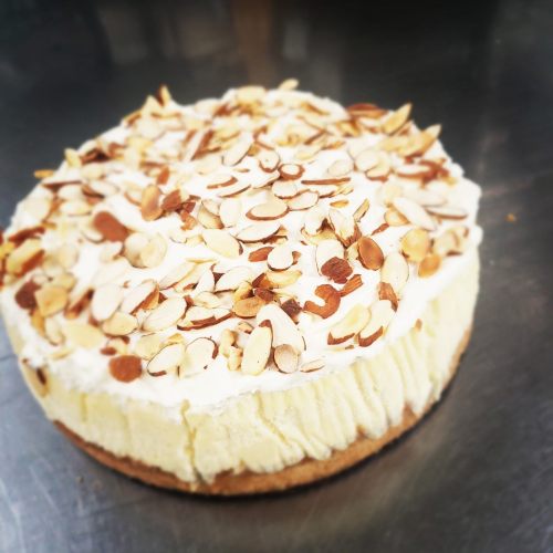 A creamy cheesecake topped with sliced almonds on a silver surface.