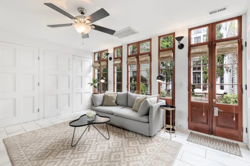 Bright living room with a gray sofa, coffee table, and large windows, featuring a ceiling fan and stylish decor.