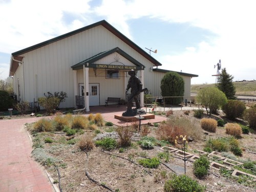 Exterior view of the Limon Heritage Museum, featuring a statue in the garden and a clear sky in the background.