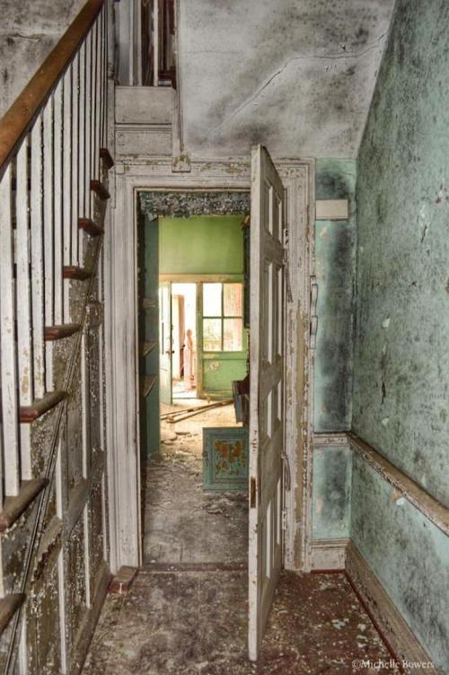 An open door reveals a dusty, abandoned interior with peeling walls and a staircase leading up.