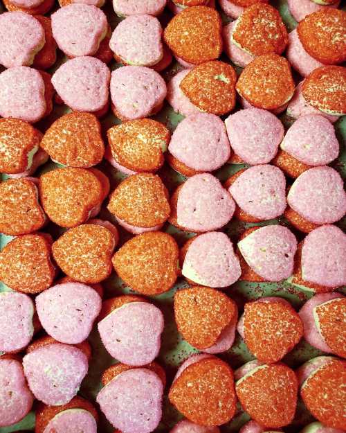 A colorful array of heart-shaped cookies in pink and orange, sprinkled with sugar and arranged neatly.