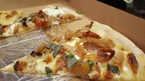 A slice of pizza topped with roasted vegetables, herbs, and melted cheese, resting in a pizza box.