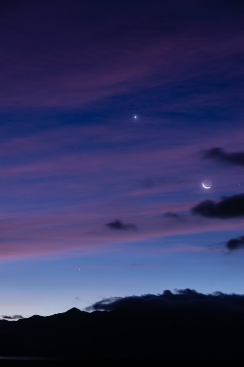 A twilight sky with soft purple and blue hues, featuring a crescent moon and bright stars among scattered clouds.