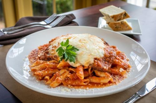 A plate of pasta with marinara sauce, topped with melted cheese and a sprig of parsley, served with garlic bread.