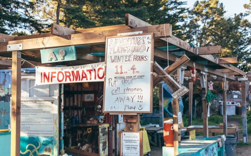 A colorful outdoor information booth with signs about winter hours and cell phone policies at an adventure playground.