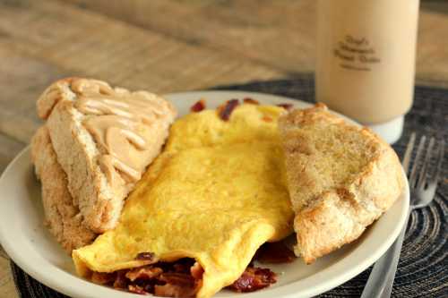 A plate with a fluffy omelet, two slices of toast with peanut butter, and a drink in the background.