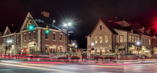 A charming town square at night, featuring festive lights and decorated buildings with holiday wreaths.