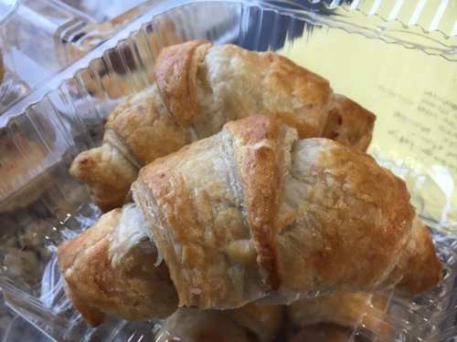 Two golden-brown croissants in a clear plastic container, showcasing their flaky, buttery layers.