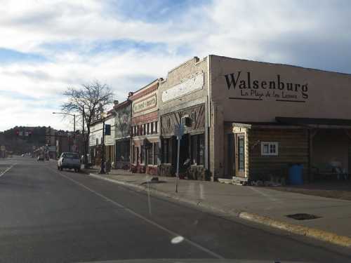 A street view of Walsenburg, featuring historic buildings and shops under a cloudy sky.