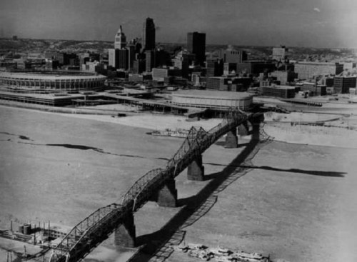 Aerial view of a city skyline with a bridge over a frozen river, surrounded by snow-covered land.