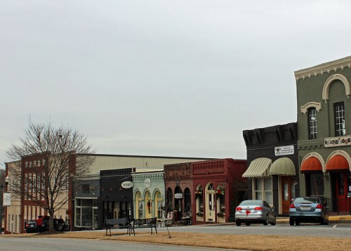 A row of charming storefronts in a small town, featuring various colors and architectural styles under a cloudy sky.