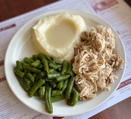 A plate with mashed potatoes, shredded chicken, and green beans on a table with a menu underneath.