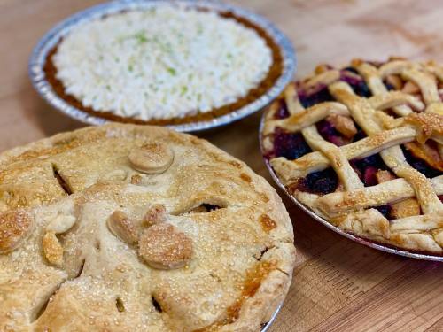 Three delicious pies on a wooden surface: a fruit pie, a cream pie, and a golden-brown pie with decorative crust.