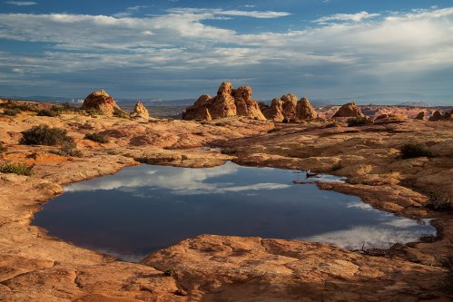A serene landscape featuring rock formations and a reflective pool of water under a cloudy sky.