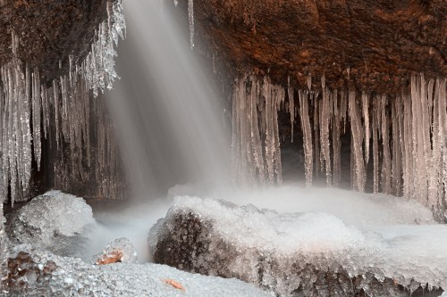 A frozen cave with icicles hanging from the ceiling and a waterfall cascading over icy rocks.
