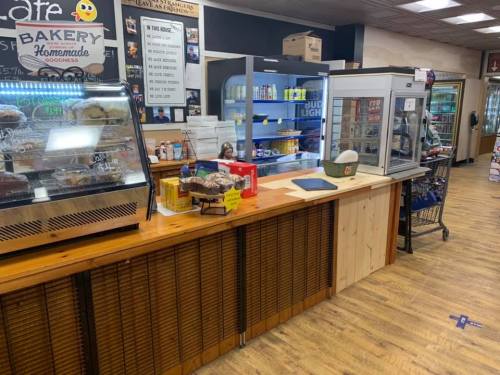 A cozy café counter with baked goods, drinks in coolers, and a wooden surface in a warm, inviting space.
