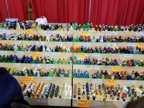 A display of colorful LEGO minifigures arranged on shelves, with price tags and signs asking not to touch.