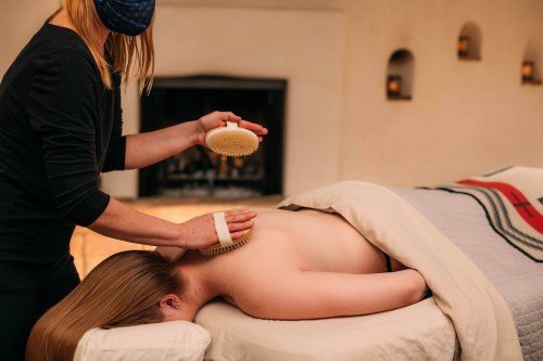 A person receives a back treatment while lying on a massage table, covered with a blanket, in a serene setting.