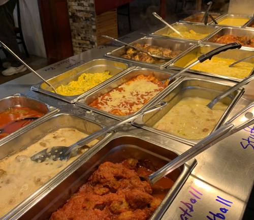 A buffet display with various trays of food, including meatballs, pasta, and creamy dishes, all served with serving utensils.