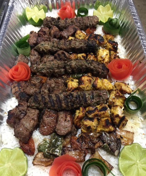 A platter of assorted grilled meats, including kebabs and chicken, served on a bed of rice with decorative vegetables.