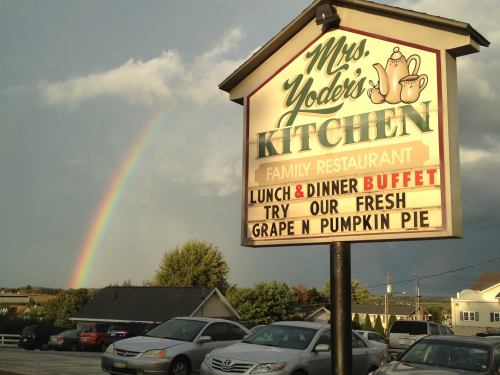 Sign for Mrs. Yoder's Kitchen restaurant with a rainbow in the background, promoting lunch and dinner buffet.