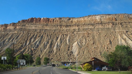A scenic view of a rocky cliffside with a clear blue sky, alongside a road and a small building in the foreground.