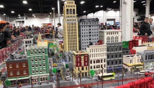 A detailed LEGO cityscape with various buildings, streets, and miniature vehicles, displayed at an event.