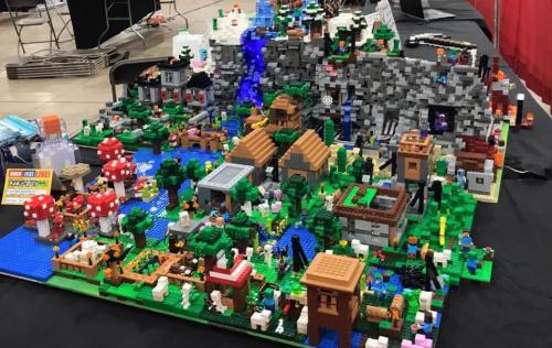 A colorful LEGO display featuring a detailed landscape with buildings, trees, water, and various characters.