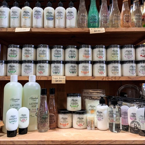 A display of various bottles and jars of soaps, scrubs, and laundry products on wooden shelves.