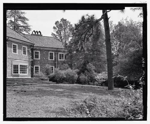 Historic stone house with a tiled roof, surrounded by trees and greenery, featuring a large patio area.