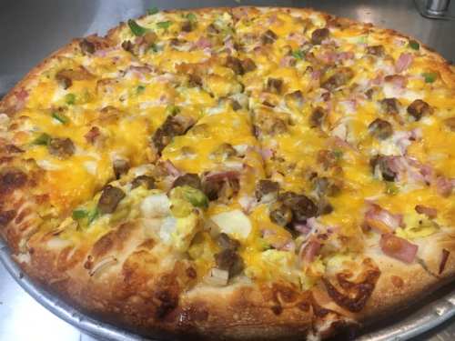 A close-up of a pizza topped with cheese, ham, green peppers, and sausage on a golden crust.