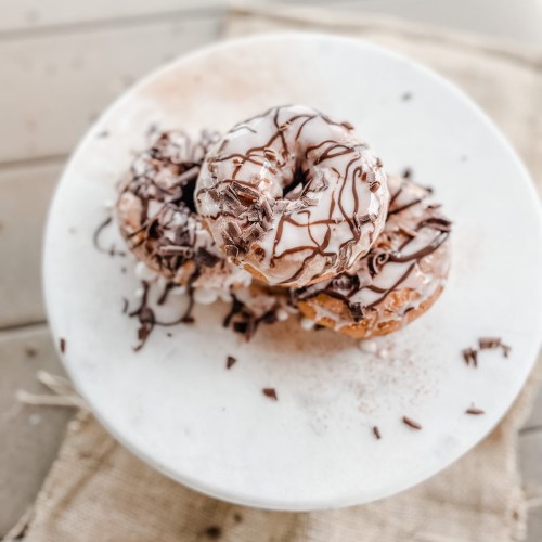 Three delicious donuts topped with chocolate icing and shavings, arranged on a white plate.
