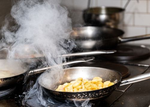 Steam rises from a pan of cooking gnocchi on a busy stovetop with multiple pots and pans in the background.