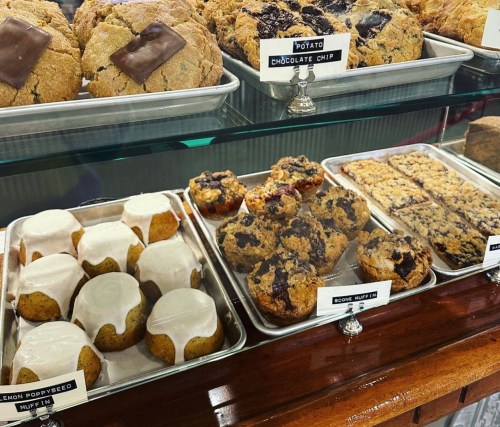 A display case filled with various baked goods, including cookies and muffins, some topped with icing.