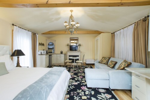 Cozy hotel room with a king bed, seating area, kitchenette, and elegant decor featuring a floral rug and chandelier.