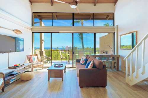 Bright, modern living room with large windows, a sofa, and a dining area, overlooking a scenic outdoor view.