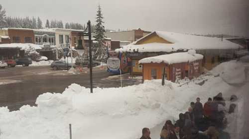 Snow-covered street scene with buildings and people gathered, set in a winter landscape.