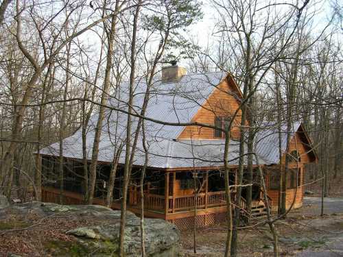 A rustic wooden cabin surrounded by bare trees and rocky terrain, featuring a sloped roof and a porch.