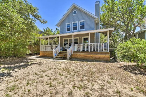 A two-story blue house with a front porch, surrounded by trees and sandy ground.