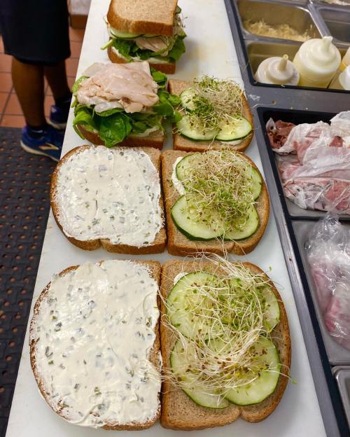 A countertop with sandwich ingredients: bread, turkey, lettuce, cucumber, sprouts, and spread arranged for assembly.