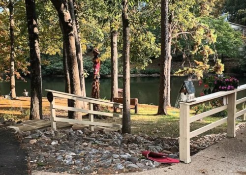 A serene lakeside scene with trees, a wooden ramp, and a small house decoration near the water.