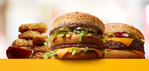 Two burgers with sesame seed buns, cheese, pickles, and lettuce, alongside a pile of chicken nuggets and dipping sauce.