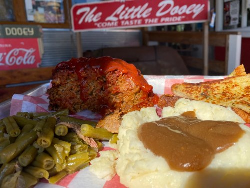 A plate featuring meatloaf with ketchup, mashed potatoes with gravy, green beans, and toasted bread at a diner.